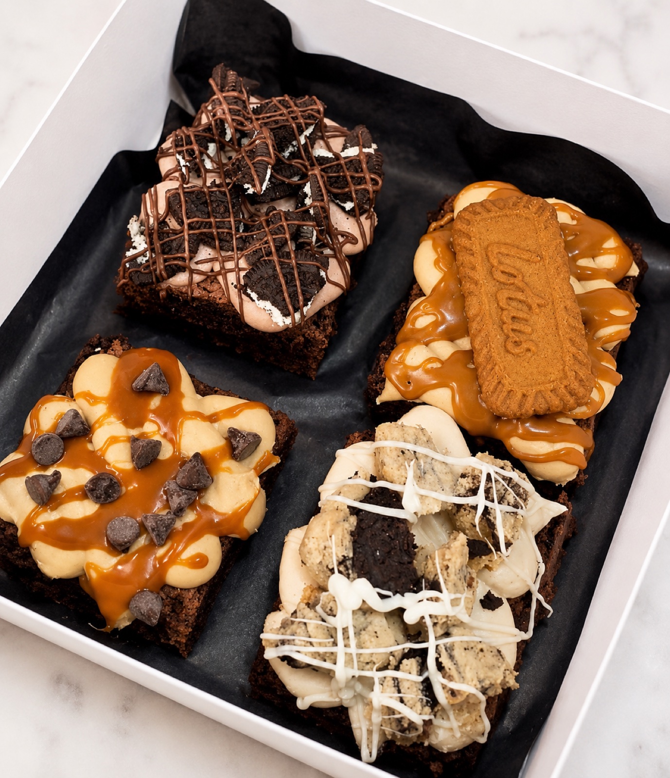 Four decorated gourmet brownies arranged in a gift box