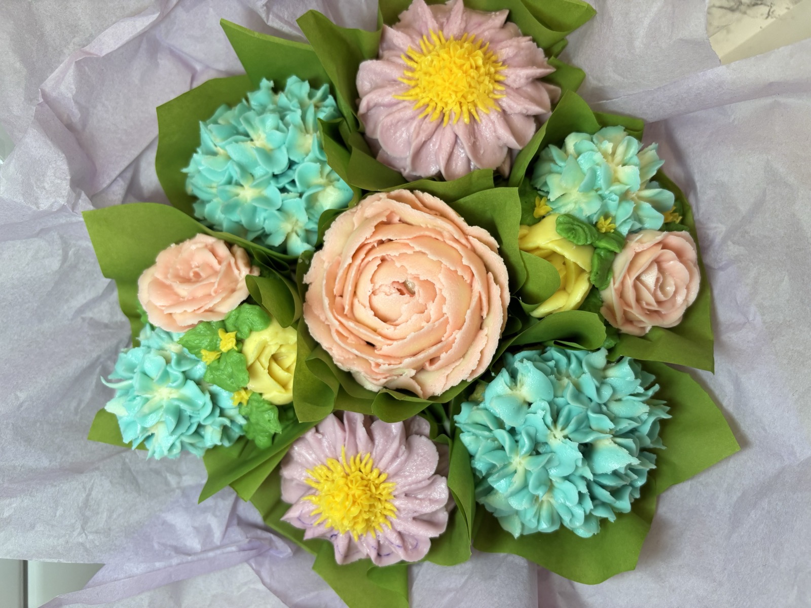 Blue, pink, and yellow blooming cupcakes arranged in a bouquet